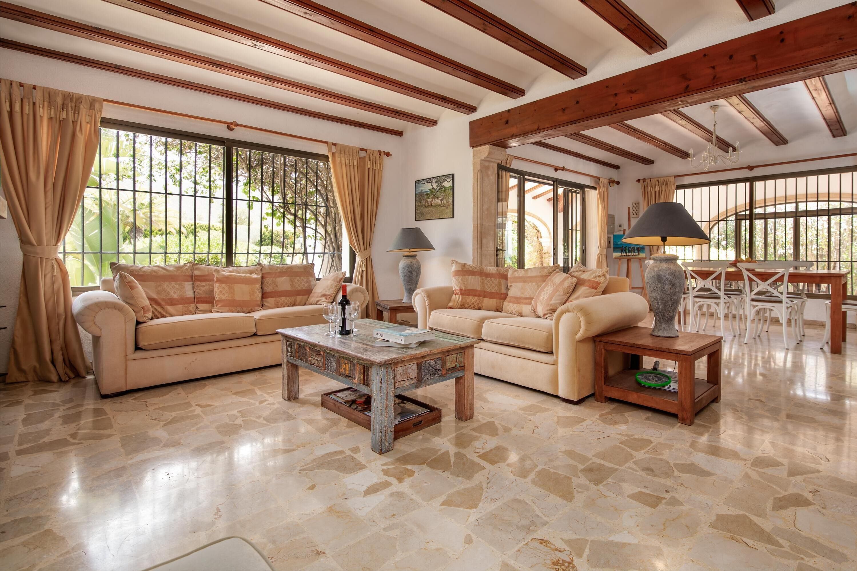 A spacious living room with two beige sofas, a coffee table, and a dining area with a white table and chairs.