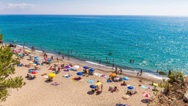 Een strand met mensen die zonnen en zwemmen, en kleurrijke parasols.