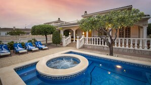 Een zwembad met jacuzzi, ligbedden en een gebouw met balkon.
