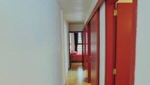 En hall med röda dörrar och en säng som syns på avstånd.