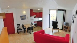Ett vardagsrum med en röd soffa, en matplats med stolar, ett kök med röda skåp och en tv-apparat placerad på ett träställ.