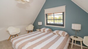 Un dormitorio con una cama, dos sillas, un ventanal y una lámpara.