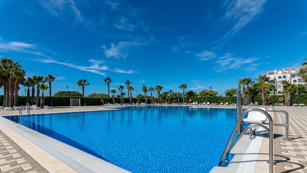 Ein rechteckiger Pool mit klarem, blauem Wasser, umgeben von Palmen und einer gefliesten Liegefläche.