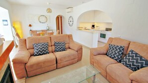 A living room with two sofas, a glass coffee table, and a kitchen in the background. - Alldo - modern hillside villa with pool & views (Moraira)