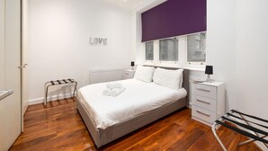 A modern bedroom with a bed, a radiator, a window with blinds, a bedside table with a lamp, and a towel rack.