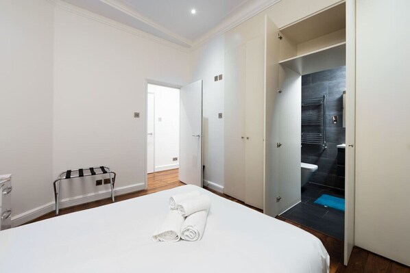A hotel room with a large bed, a bathroom with a shower, and a hallway leading to another room. - Central London Flat (FS1) (London)