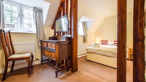 A bedroom with a wooden dresser, a chair, a bed with pillows, and a window with curtains. - A sudeley castle cottage that sleeps 4 guests  in 2 bedrooms (Cheltenham)