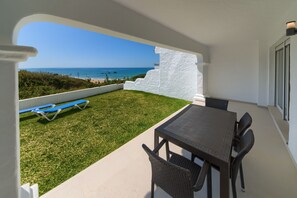 Une terrasse avec une table et des chaises, un fauteuil de jardin bleu et une vue sur l’océan.