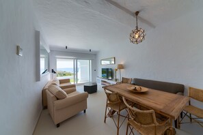 Un salon moderne avec une table à manger en bois, des chaises en osier, un canapé et un luminaire suspendu au plafond.