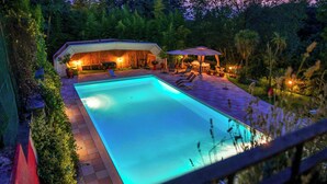 A swimming pool with a covered patio area, surrounded by lush greenery and trees.