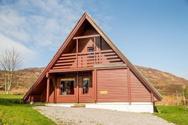 A wooden triangular building with a sloped roof, a small entrance, and a window.