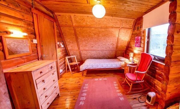 A cozy cabin room with a bed, a chair, a dresser, and a window. - Steading Holidays - Ian's Lodge (Acharacle)