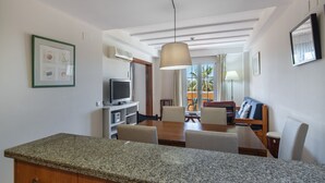 A modern kitchen with granite countertops, a dining area with a wooden table and chairs, a television, and a large window with curtains. - La Quinta de Isla Canela II - Isla Canela Golf GQHII10P10 (Isla Canela)