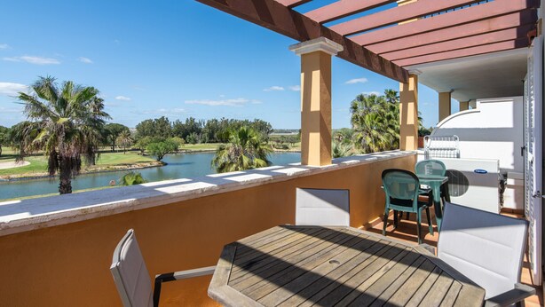 A balcony with a view of a lake, palm trees, and a grill. - La Quinta de Isla Canela II - Isla Canela Golf GQHII10P10 (Isla Canela)