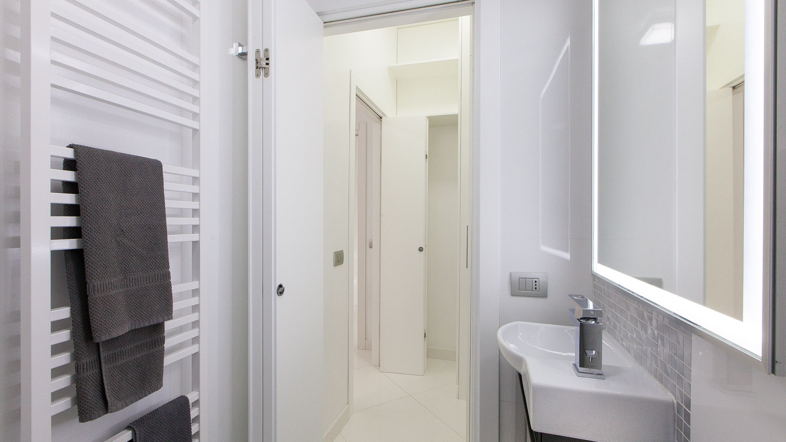 A modern bathroom with a white sink, a large mirror, and a towel rack with multiple towels.