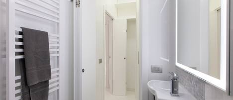 A modern bathroom with a white sink, a large mirror, and a towel rack with multiple towels.