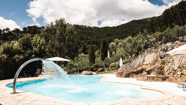 A swimming pool with a waterfall feature, surrounded by a stone wall and a grassy area.