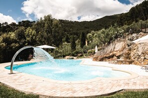 Une piscine agrémentée d’une cascade, entourée d’un mur de pierre et d’une pelouse.