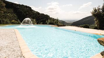 Relax by the serene pool surrounded by lush green hills and a soothing water feature.