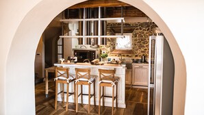 A kitchen with a central island, bar stools, a stone wall, and a rustic wooden ceiling.
