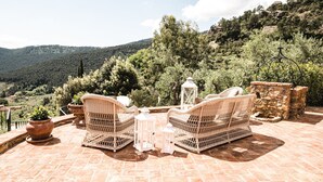 A terrace with wicker furniture and stone walls, overlooking a mountainous landscape.