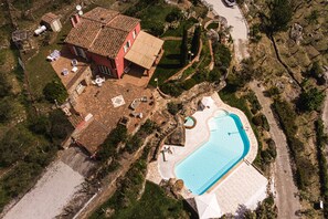 Vue aérienne d’une propriété dotée d’une piscine, d’un bâtiment rouge et d’un jardin bien entretenu.