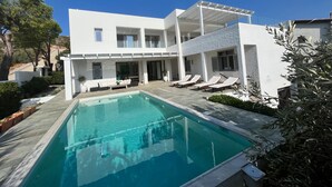 A modern two-story building with a swimming pool, lounge chairs, and a pergola.