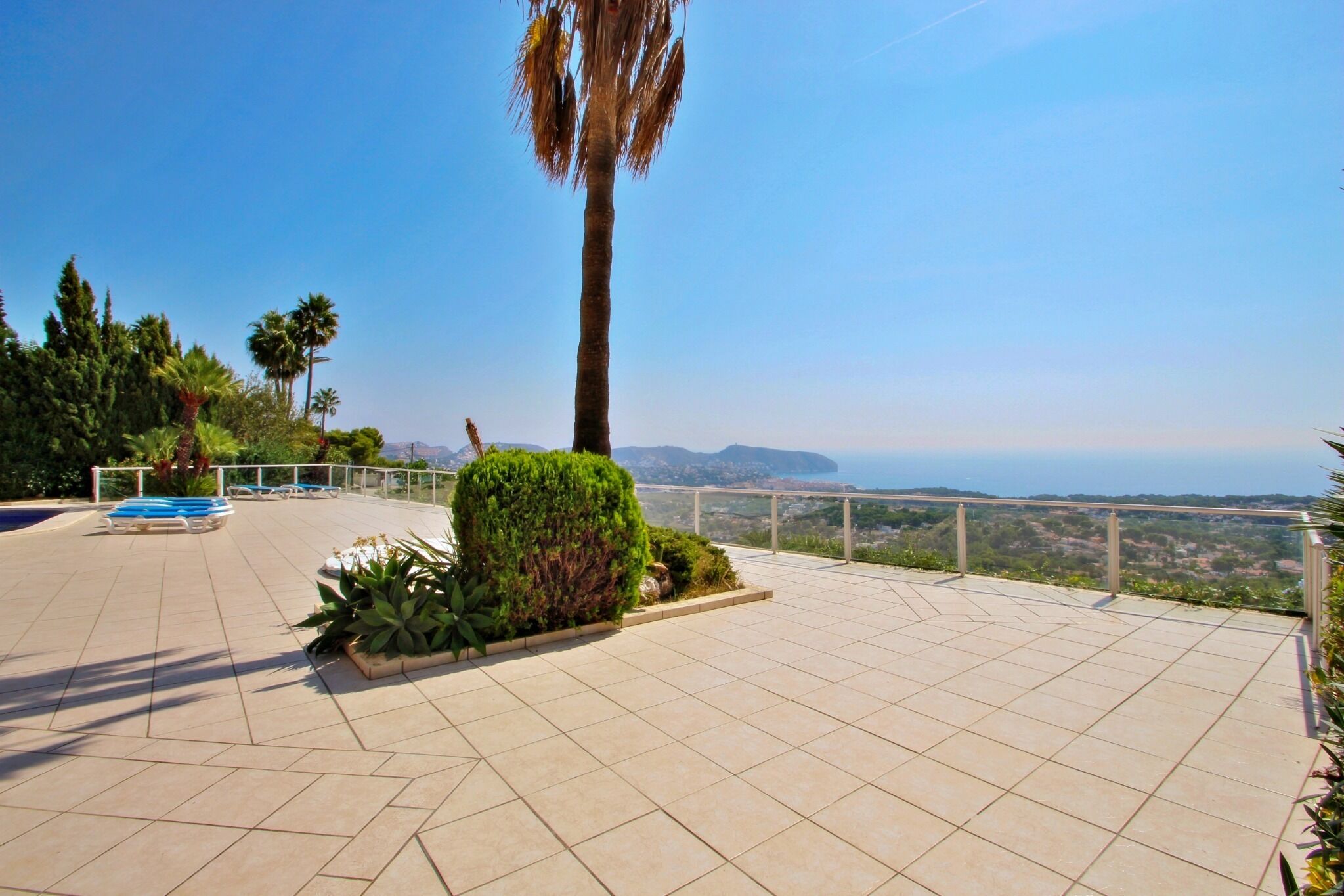 A terrace with tiled flooring, a palm tree, and a view of the coastline.