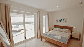 Habitación de hotel con una cama, una mesita de noche, un cuadro en la pared y vistas al exterior a través de amplios ventanales correderas.