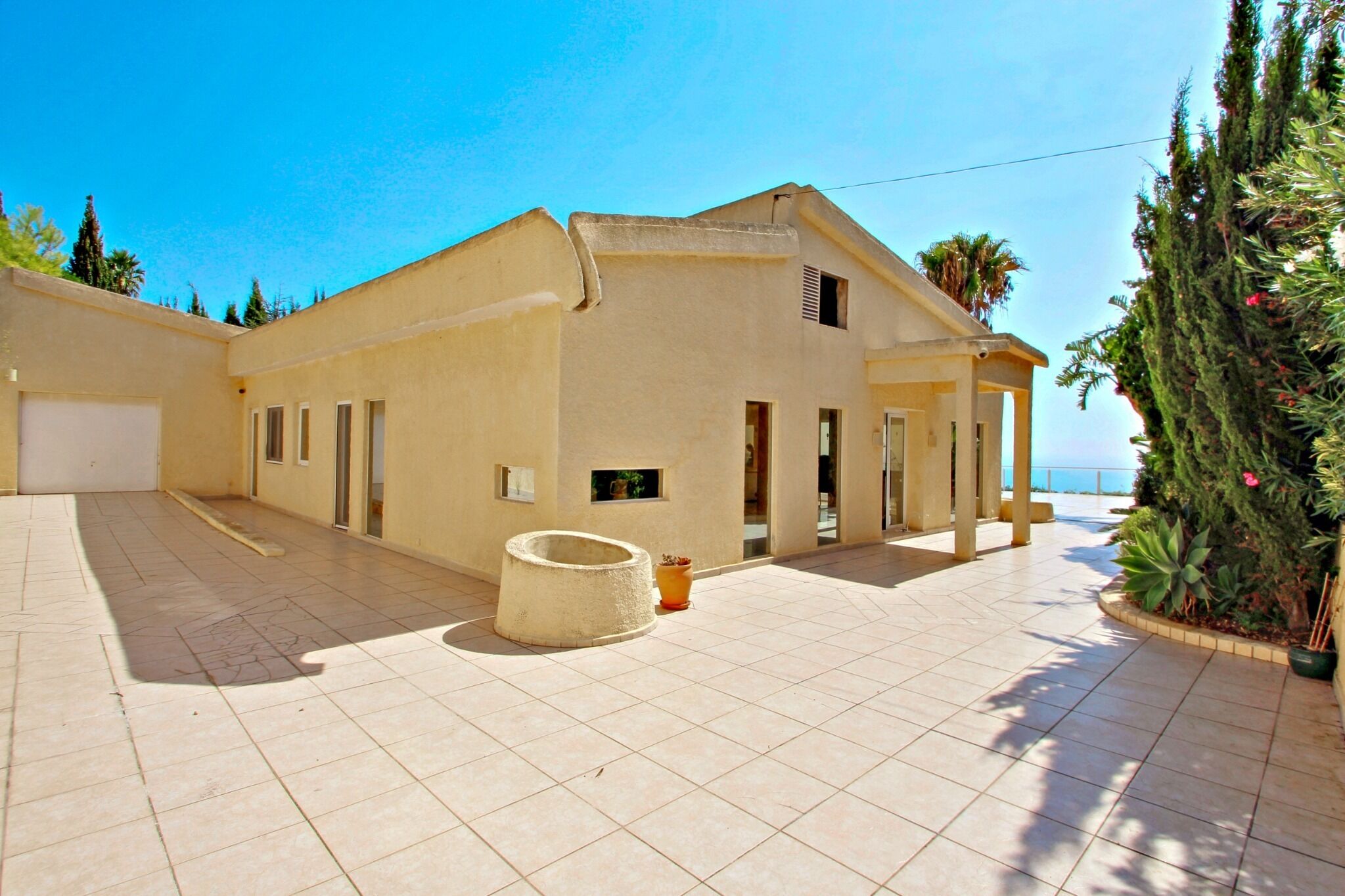 A spacious building with a tiled courtyard, a covered outdoor seating area, and a view of the sea.