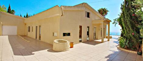 A spacious building with a tiled courtyard, a covered outdoor seating area, and a view of the sea.