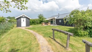 Il s’agit d’une propriété comprenant un petit abri de jardin, un espace extérieur aménagé avec un coin salon couvert, et un chemin menant à la maison.