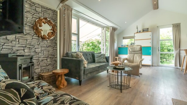 Un salon avec un mur en pierre, une cheminée, un canapé, une table basse et un coin repas comprenant une chaise et un buffet.