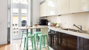 A modern kitchen with a central island, bar stools, and a view through an open door.