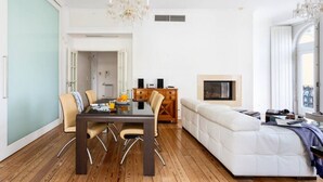 A modern living room with a white sofa, a dining table with chairs, and a chandelier.