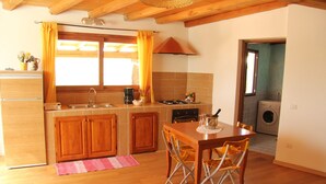 A compact kitchen with wooden cabinets, a dining table with chairs, a washing machine, and a small window with curtains. - Cosy apartment for 5 people with WIFI, private pool, A/C, TV, patio, pets allowed and panoramic ... (Olbia)