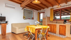 A cozy room with a wooden ceiling, a dining table with yellow chairs, a sofa, a small kitchen area, and a window with curtains. - Cosy apartment for 5 people with WIFI, private pool, A/C, TV, patio, pets allowed and panoramic ... (Olbia)