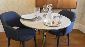 A round dining table with two blue upholstered chairs, a white plate, a wine glass, a crystal decanter, and a small glass on a silver tray. - The Brewmaster's House 3 | Superior Studio (Porto)