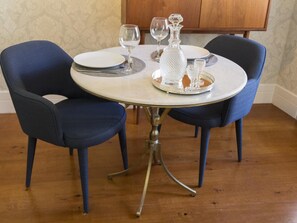 Un tavolo da pranzo rotondo con due sedie imbottite blu, un piatto bianco, un bicchiere da vino, un decantatore di cristallo e un piccolo bicchierino su un vassoio d'argento.