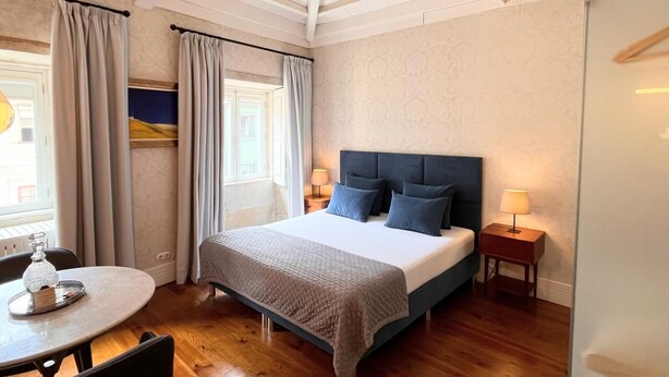 A bedroom with a bed, bedside tables, a window with curtains, a table with a glass top, and a chair. - The Brewmaster's House 3 | Superior Studio (Porto)