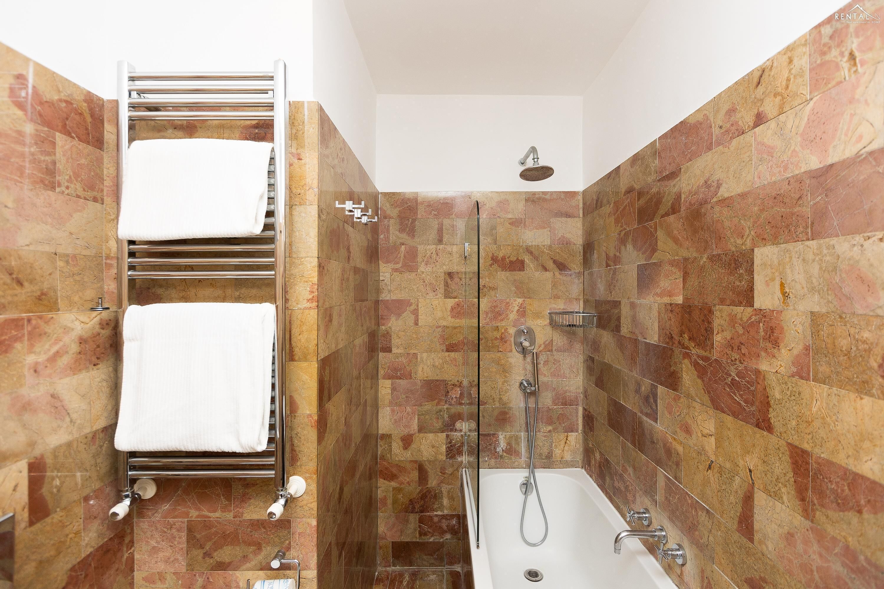 Ein Badezimmer mit einer gläsernen Duschkabine, einer weißen Badewanne und einem Handtuchhalter mit zwei Handtüchern.