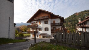 Un chalet traditionnel doté de balcons en bois, d’un mur en pierre et surplombant un paysage montagneux.