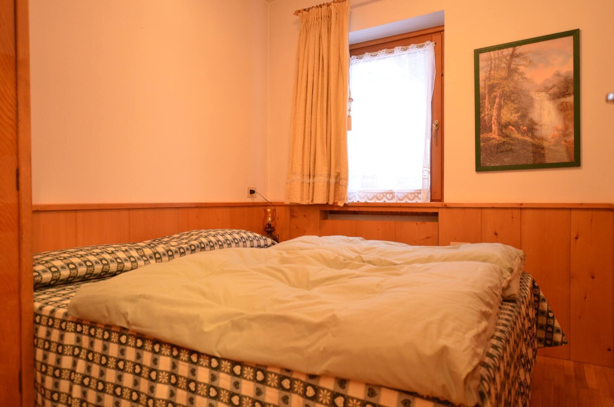 Ein Schlafzimmer mit zwei Betten, einem Fenster mit Vorhang und einem gerahmten Bild an der Wand.