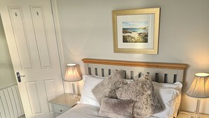 A neatly arranged bedroom with a bed, two bedside tables, a nightstand, a door, and a framed picture on the wall. - The ultimate secluded Holiday Cottage (Oban)