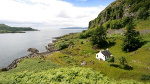 A coastal landscape with a white building on a grassy hill overlooking a body of water. - The ultimate secluded Holiday Cottage (Oban)