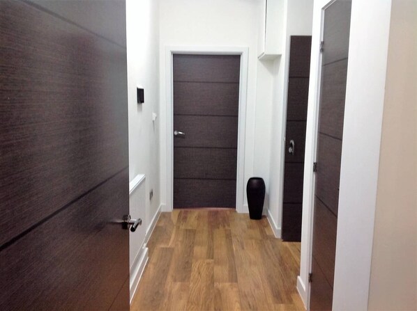 A hallway with a wooden floor, a dark door, and a black vase on the floor.