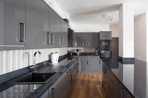 A modern kitchen with dark countertops, stainless steel appliances, and wooden flooring.