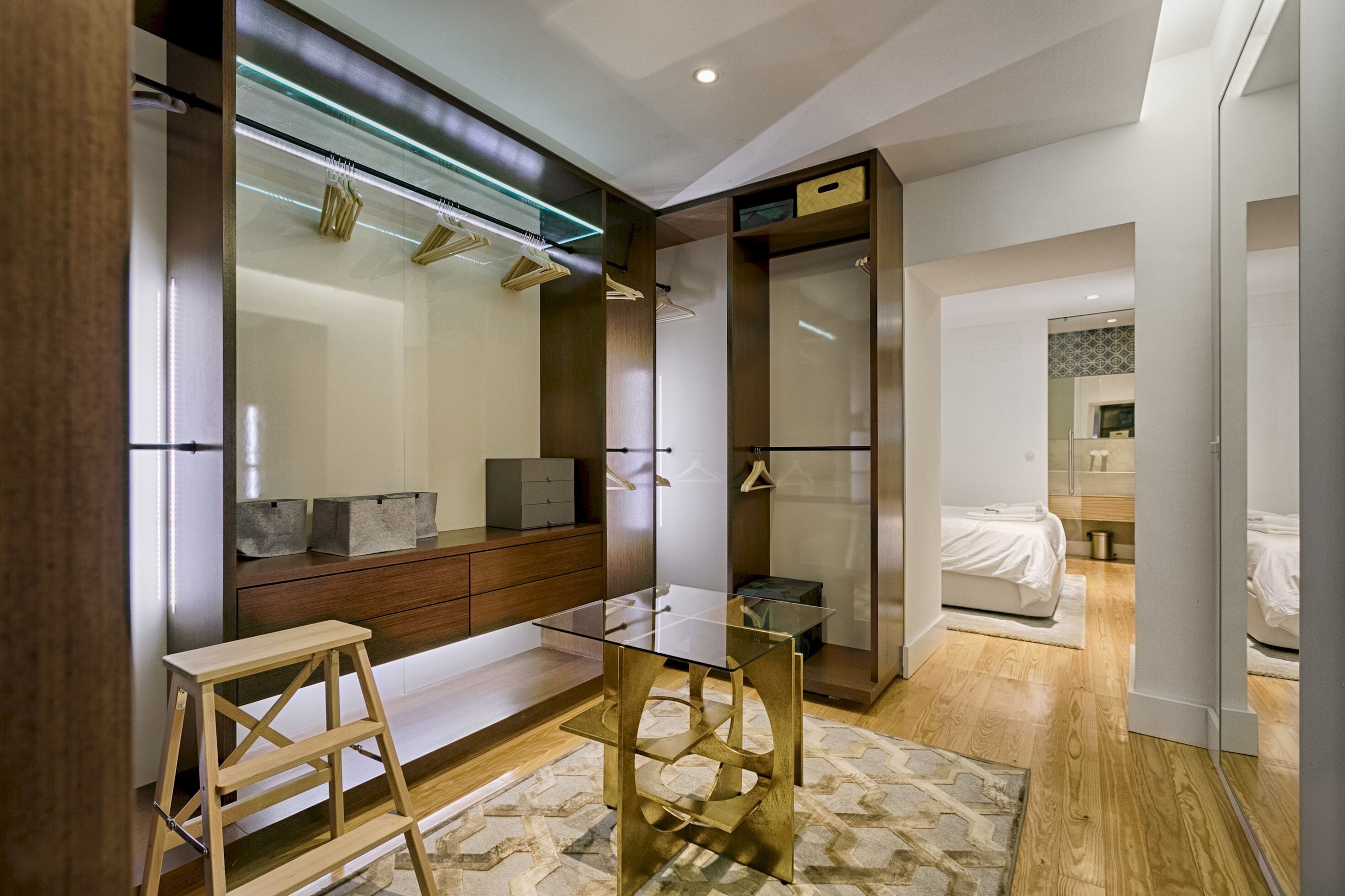 A modern bedroom with a glass desk, wooden dresser, and a walk-in closet.