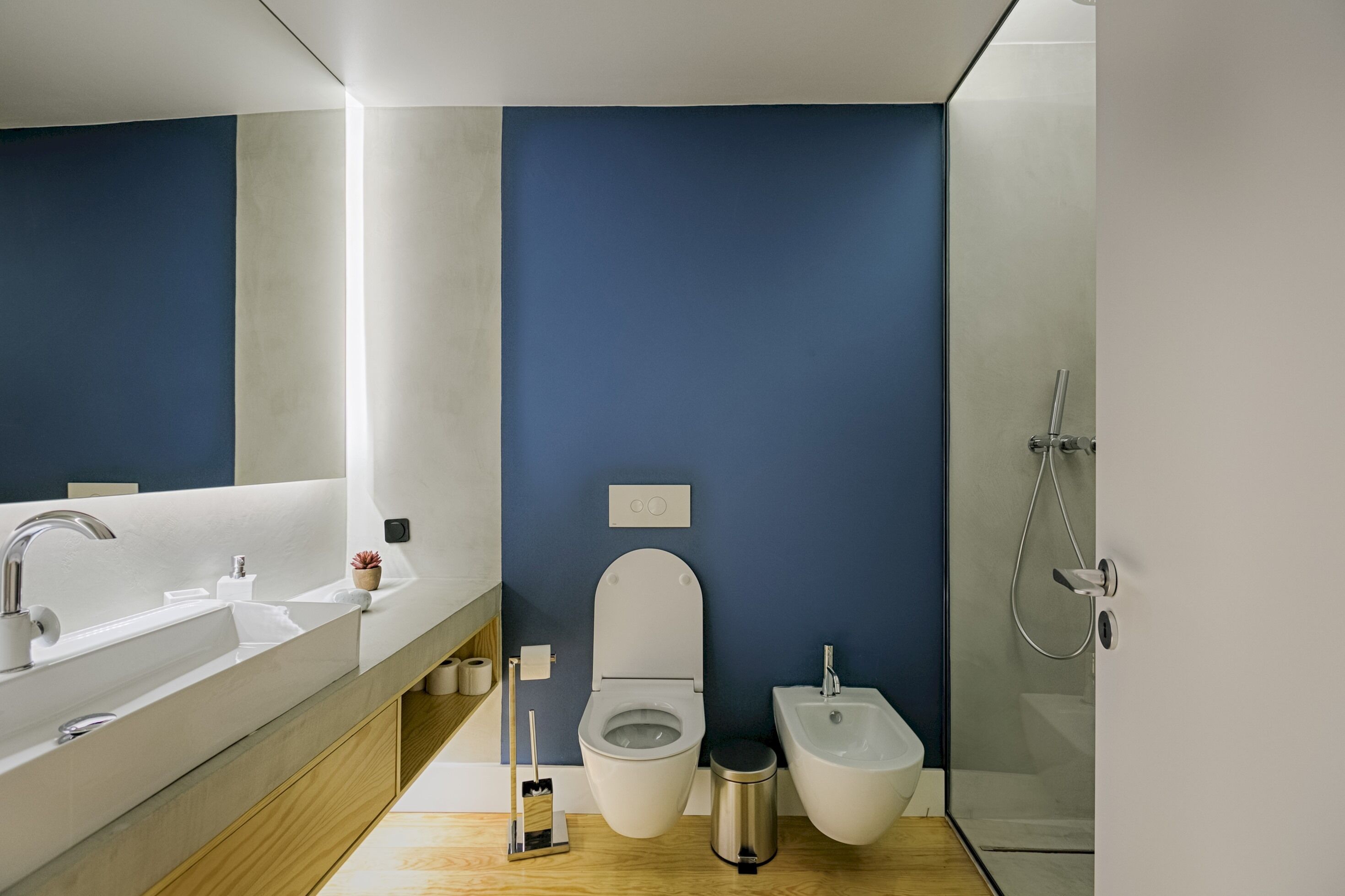A modern bathroom with a large mirror, dual sinks, a toilet, bidet, and a shower.