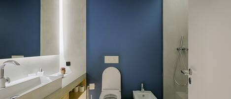 A modern bathroom with a large mirror, dual sinks, a toilet, bidet, and a shower.
